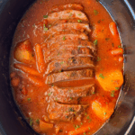 overhead shot of cooked, sliced Eye of Round Roast in a black slow cooker