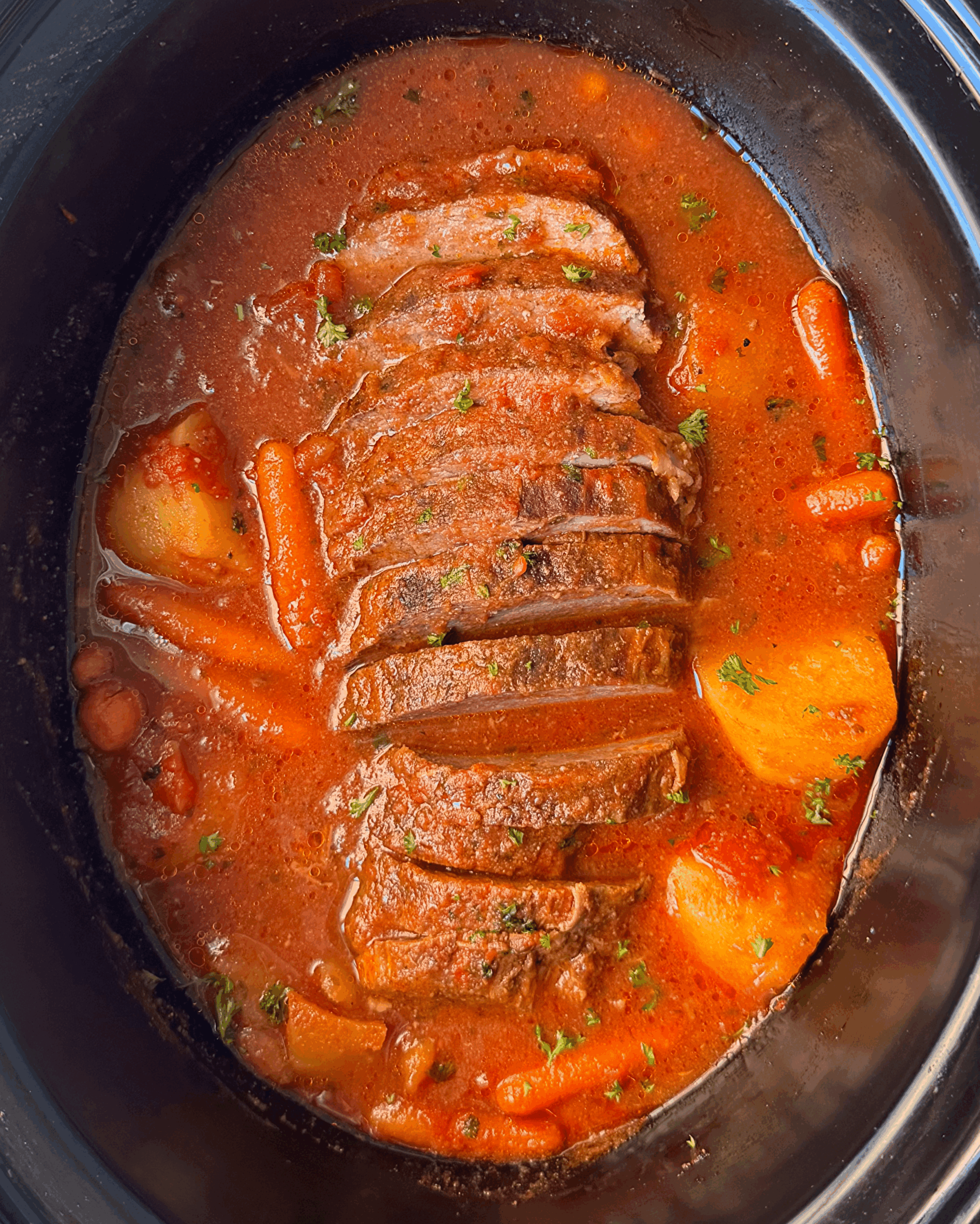 overhead shot of cooked, sliced Eye of Round Roast in a black slow cooker