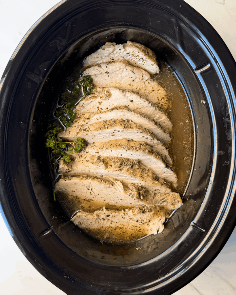 overhead shot of cooked, sliced boneless turkey breast in a black slow cooker