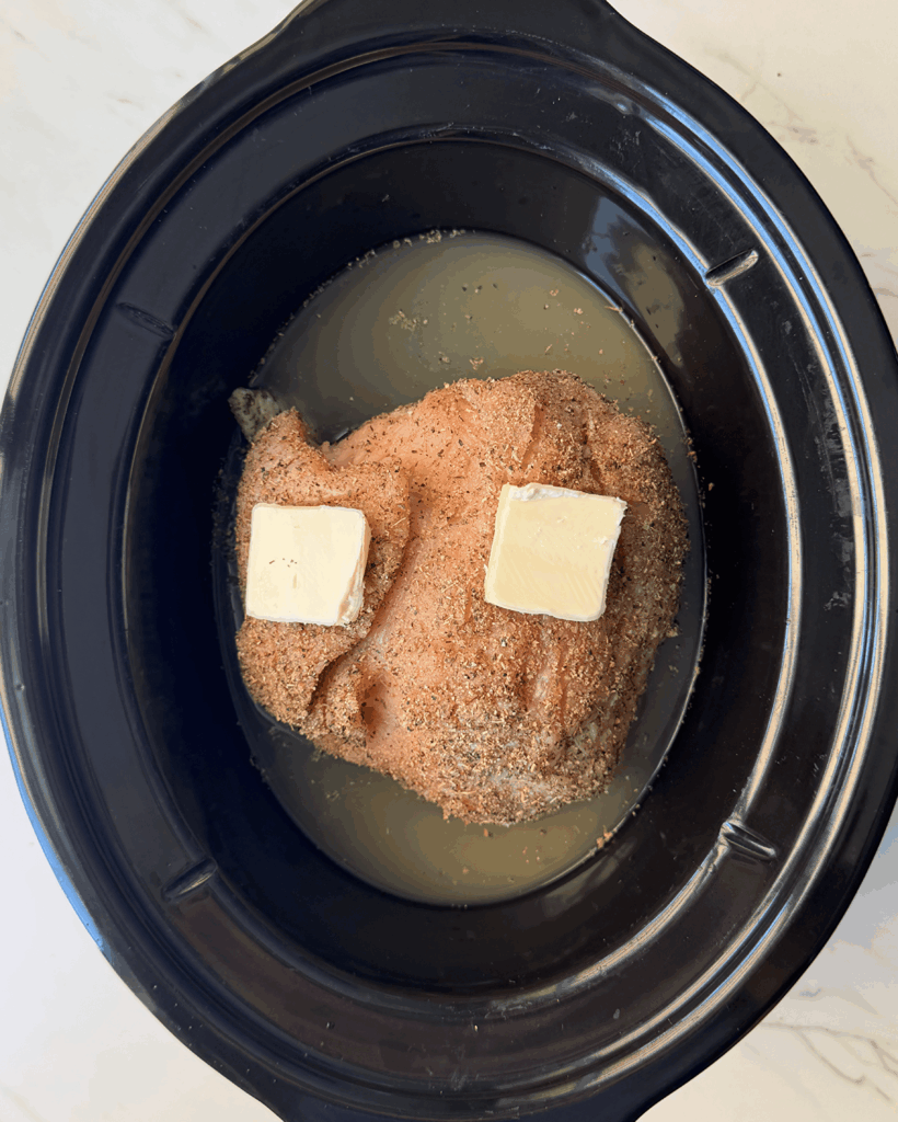 overhead shot of uncooked boneless turkey breast in a black slow cooker