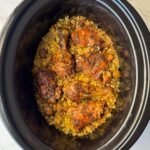 overhead shot of curry chicken and rice in a black slow cooker garnished with fresh parsley