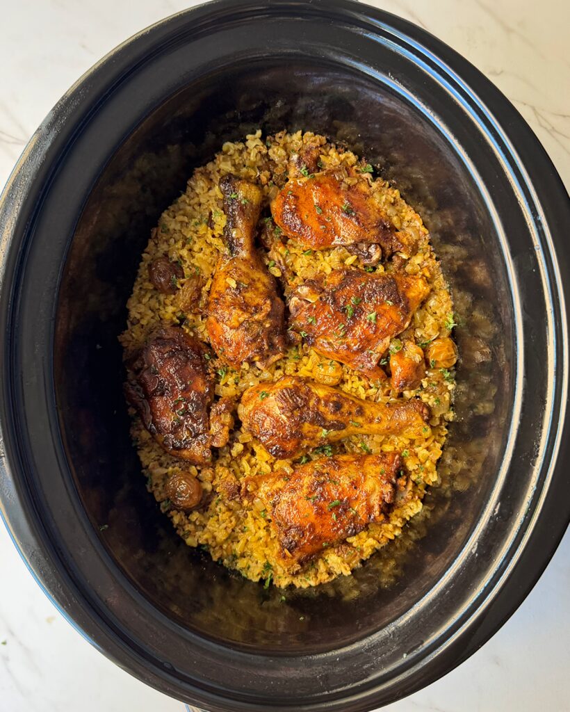 overhead shot of curry chicken and rice in a black slow cooker garnished with fresh parsley