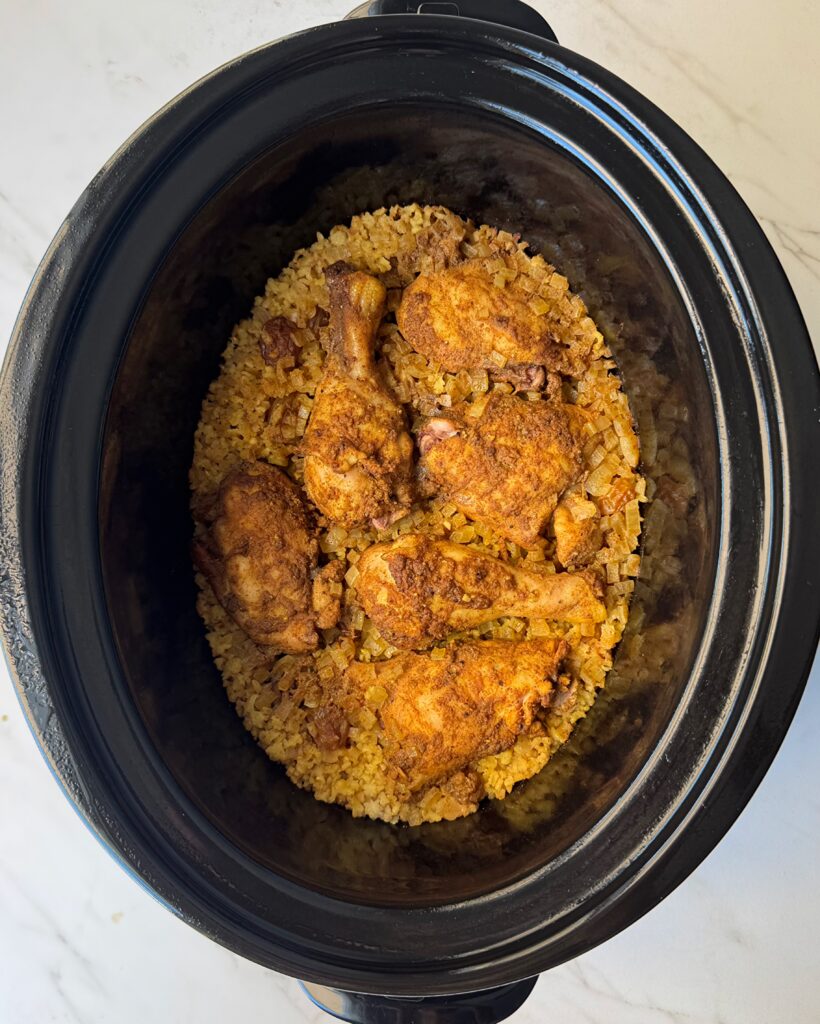overhead shot of cooked curry chicken and rice in a black slow cooker garnished with fresh parsley