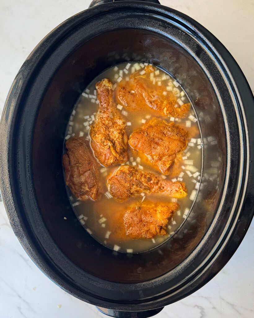 overhead shot of uncooked curry chicken and rice in a black slow cooker garnished with fresh parsley