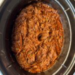 overhead shot of cooked, shredded BBQ Beef in a black slow cooker