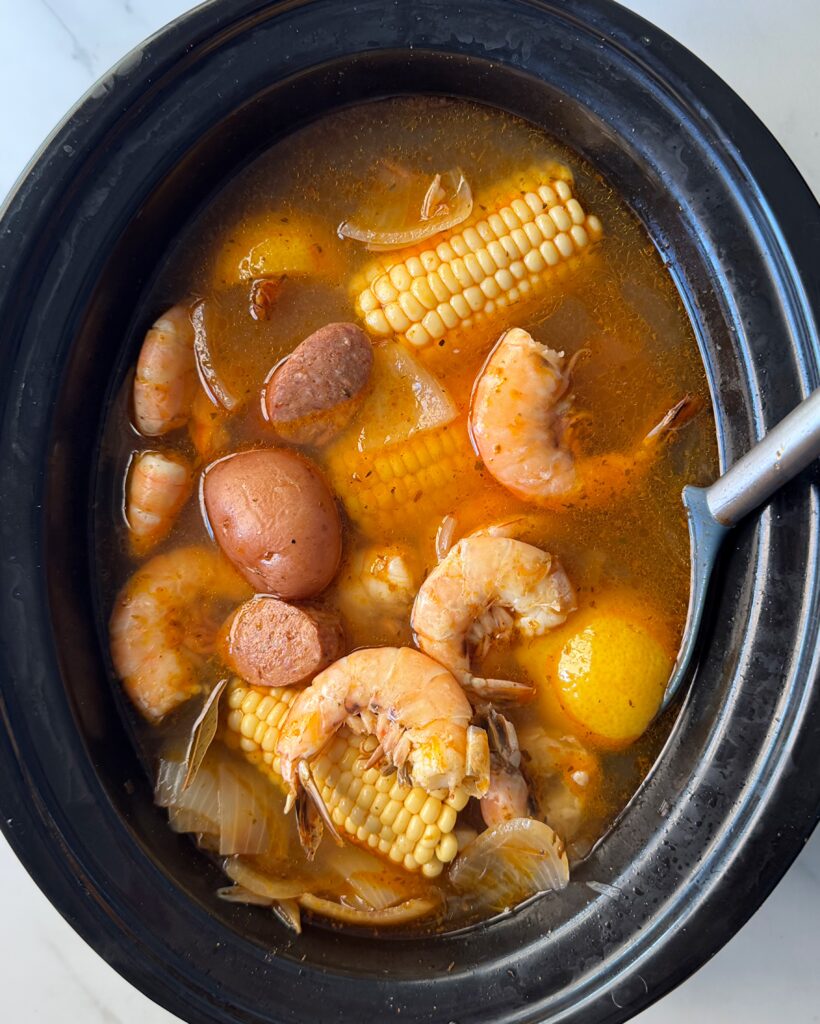 overhead shot of cooked shrimp boil in a black slow cooker with the shrimp