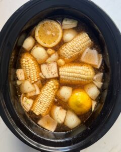 overhead shot of uncooked shrimp boil in a black slow cooker without the shrimp