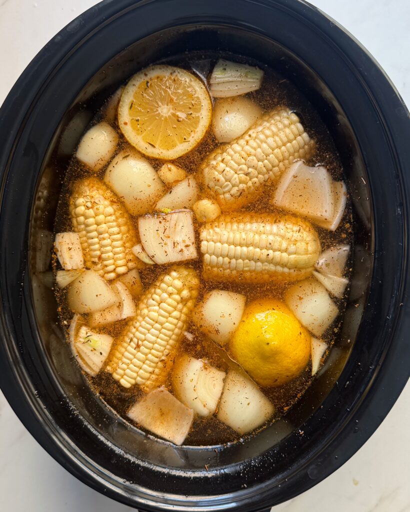 overhead shot of uncooked shrimp boil in a black slow cooker without the shrimp