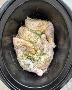 overhead shot of uncooked chicken leg quarters in a black slow cooker