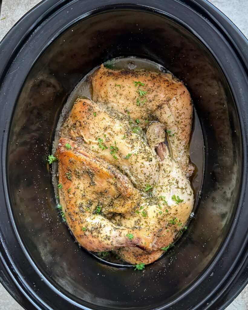 overhead shot of cooked chicken leg quarters in a black slow cooker