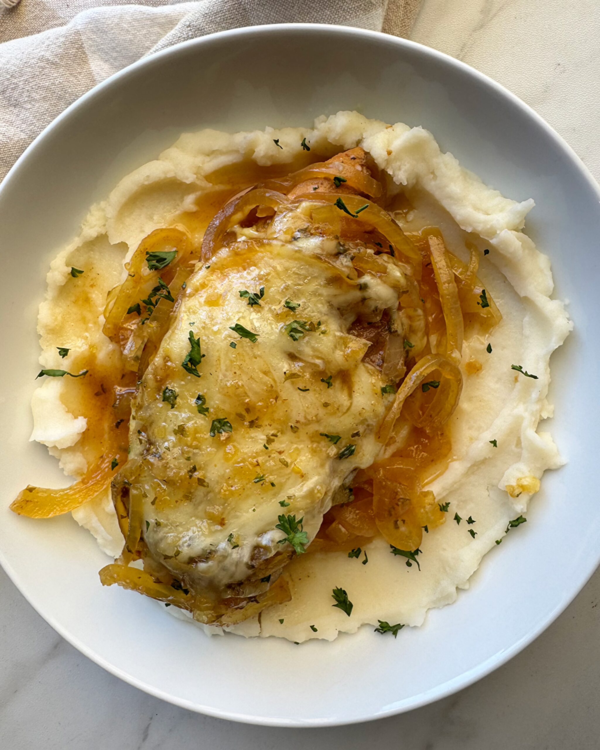 overhead shot of Crockpot French Onion Chicken served over mashed potatoes on a white plate