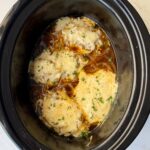 overhead shot of cooked French Onion Chicken in a black slow cooker with melted cheese on top