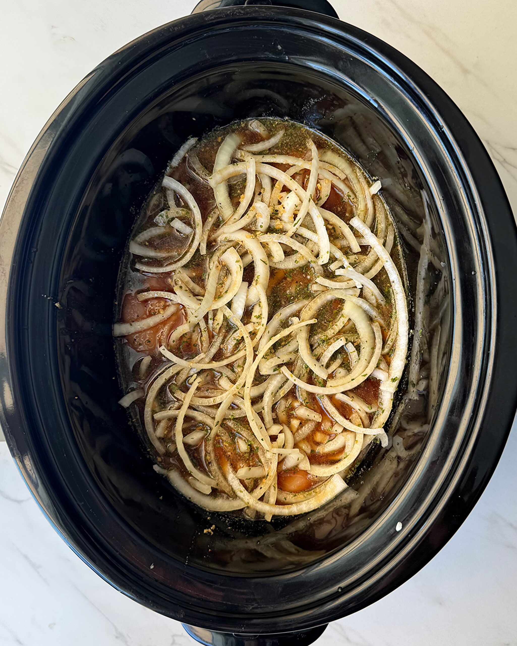 overhead shot of uncooked French Onion Chicken in a black slow cooker