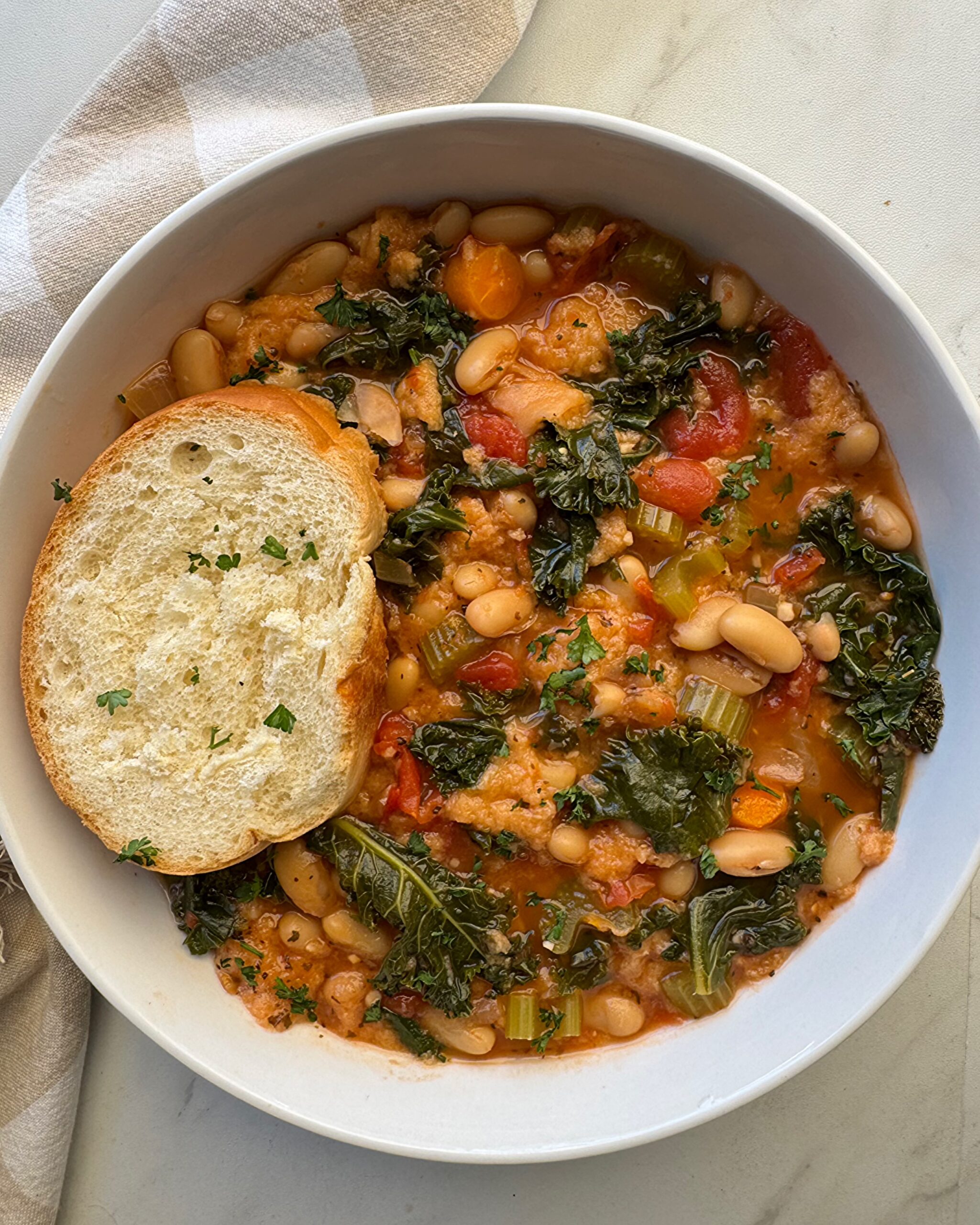 overhead shot of cooked ribollita in a white bowl with a slice of bread 