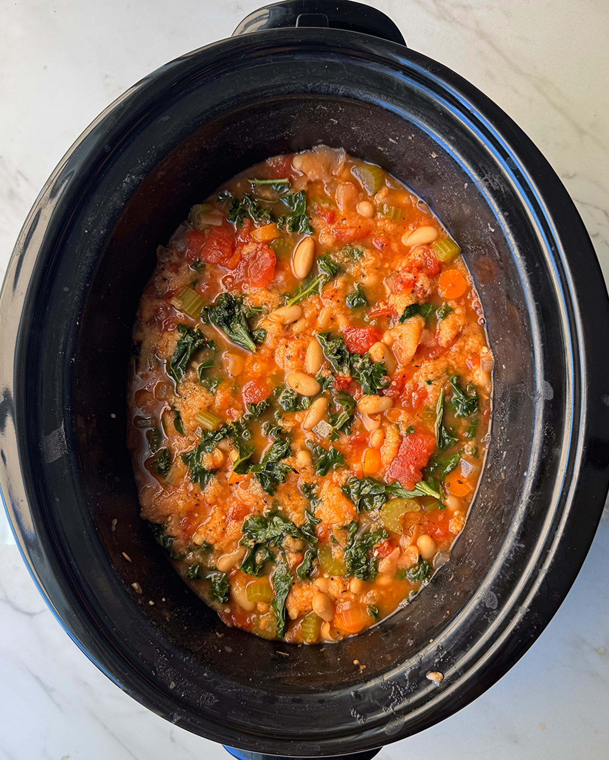 overhead shot of cooked ribollita in a black slow cooker with bread added