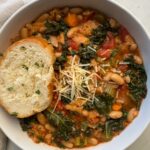 overhead shot of cooked ribollita in a white bowl with a slice of bread and garnished with grated Parmesan cheese on top