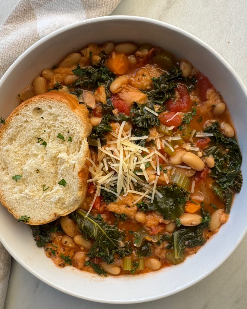 overhead shot of cooked ribollita in a white bowl with a slice of bread and garnished with grated Parmesan cheese on top