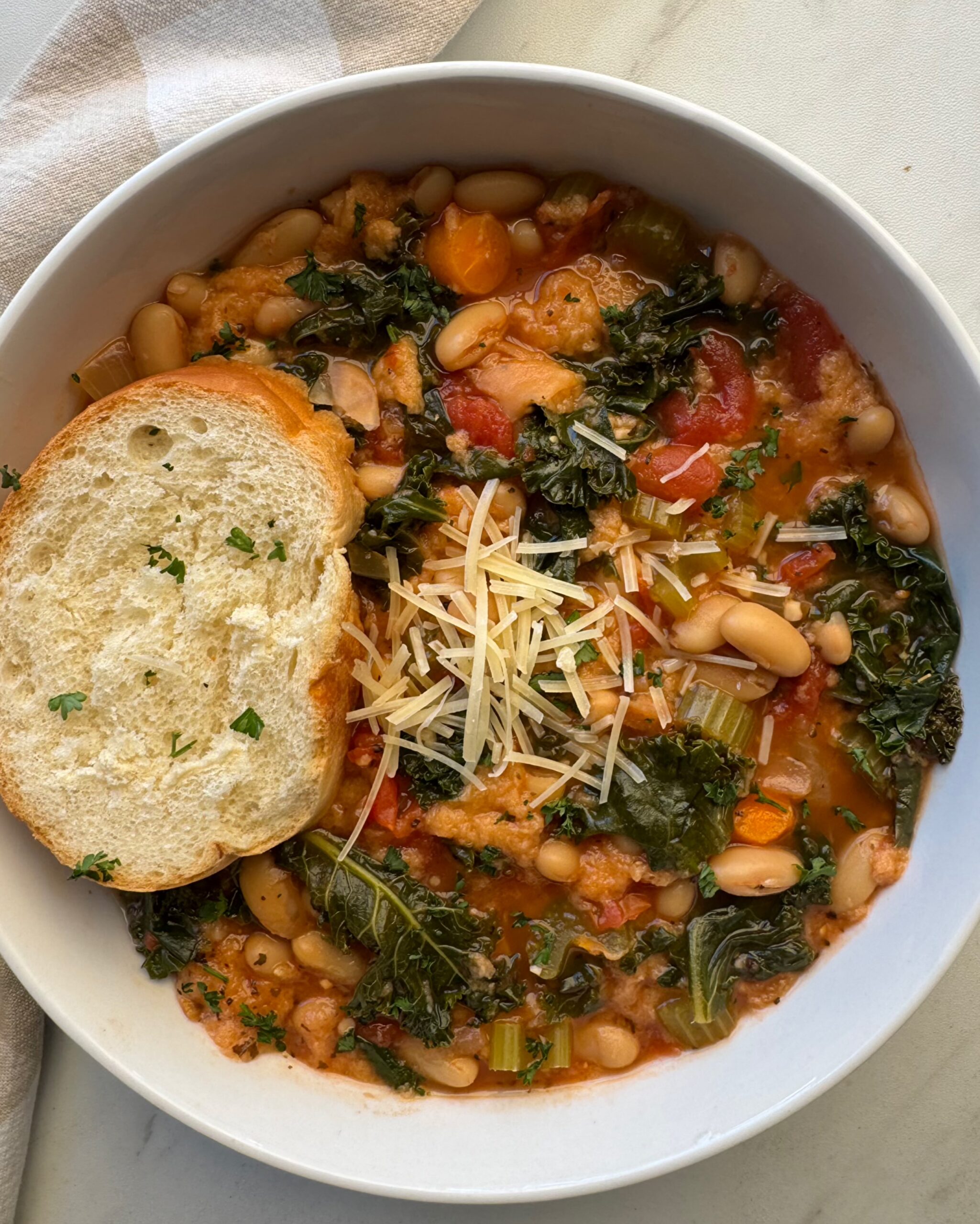 overhead shot of cooked ribollita in a white bowl with a slice of bread and garnished with grated Parmesan cheese on top