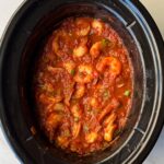 overhead shot of uncooked shrimp Creole in a black slow cooker with large shrimp