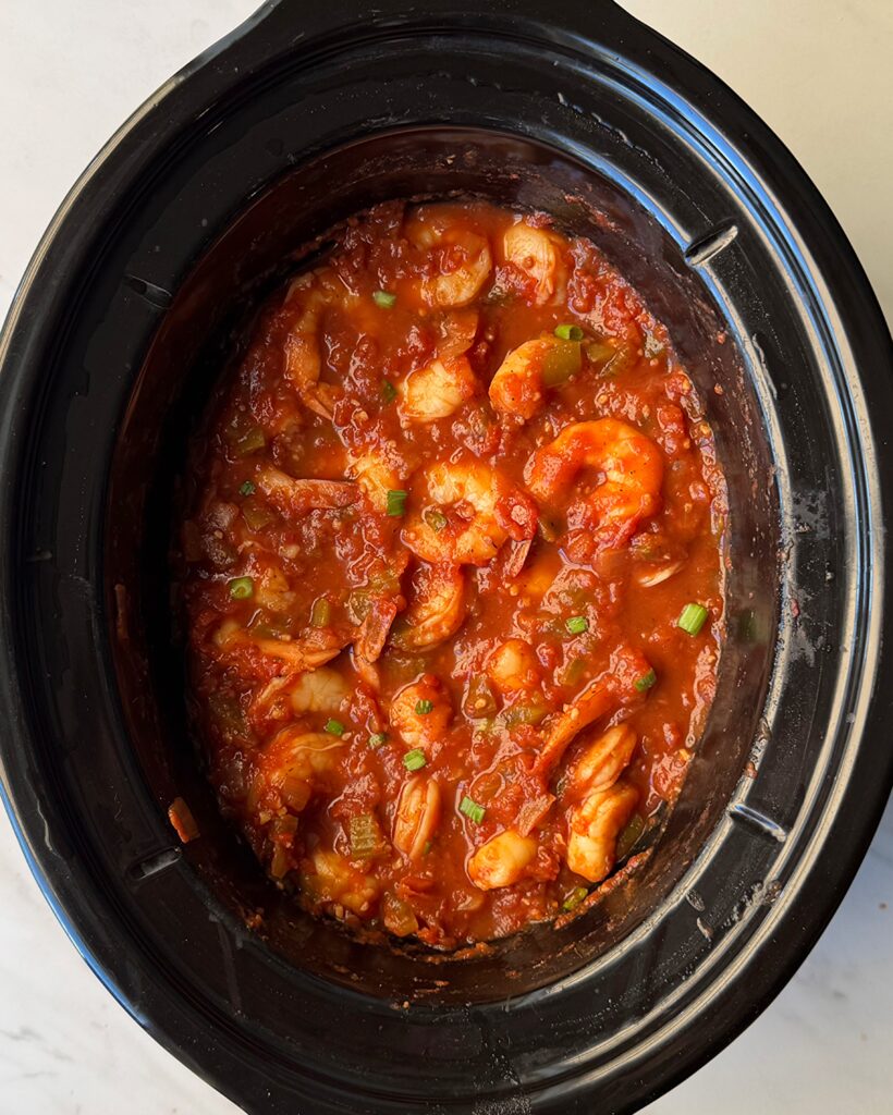 overhead shot of uncooked shrimp Creole in a black slow cooker with large shrimp