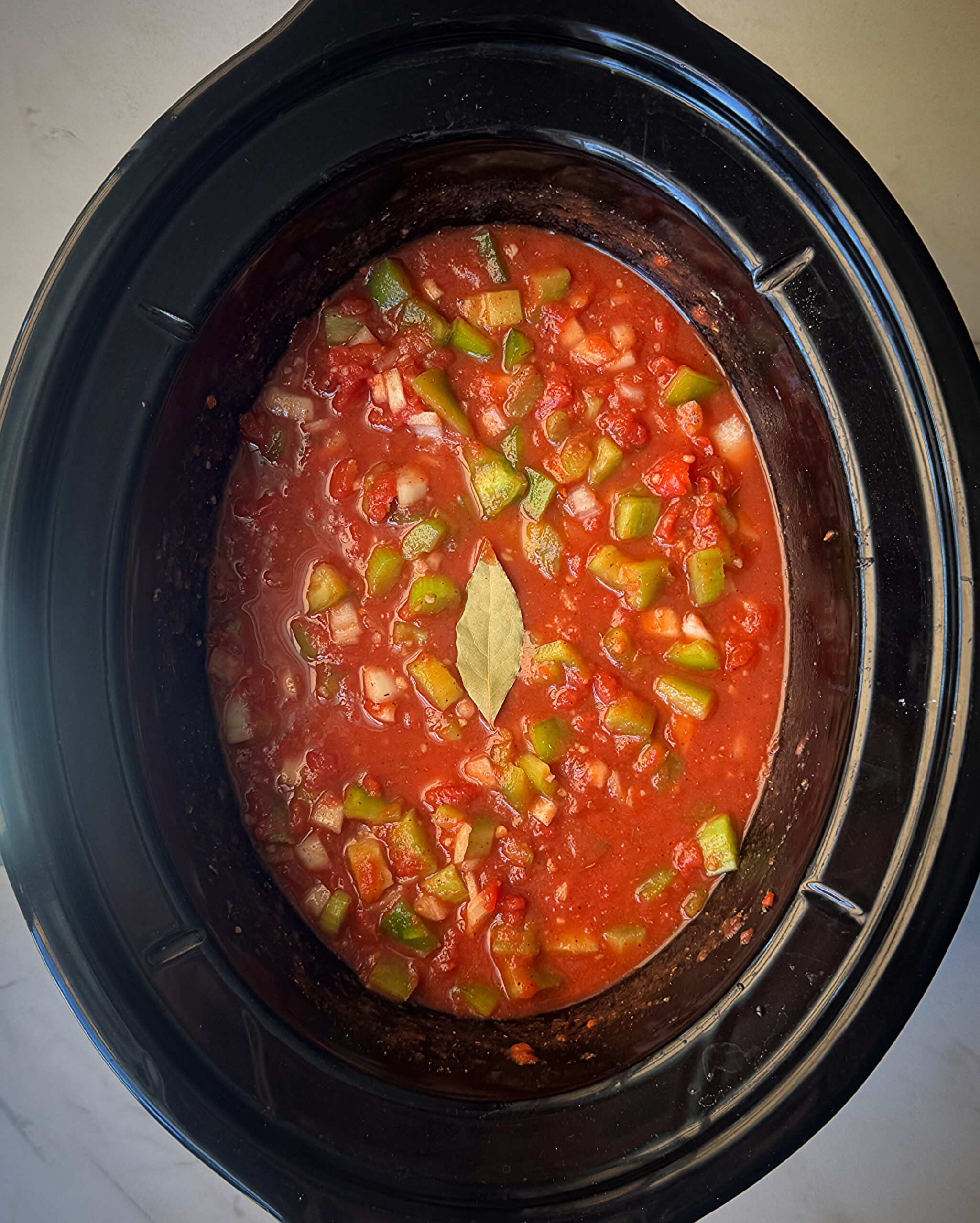 overhead shot of uncooked shrimp Creole in a black slow cooker
