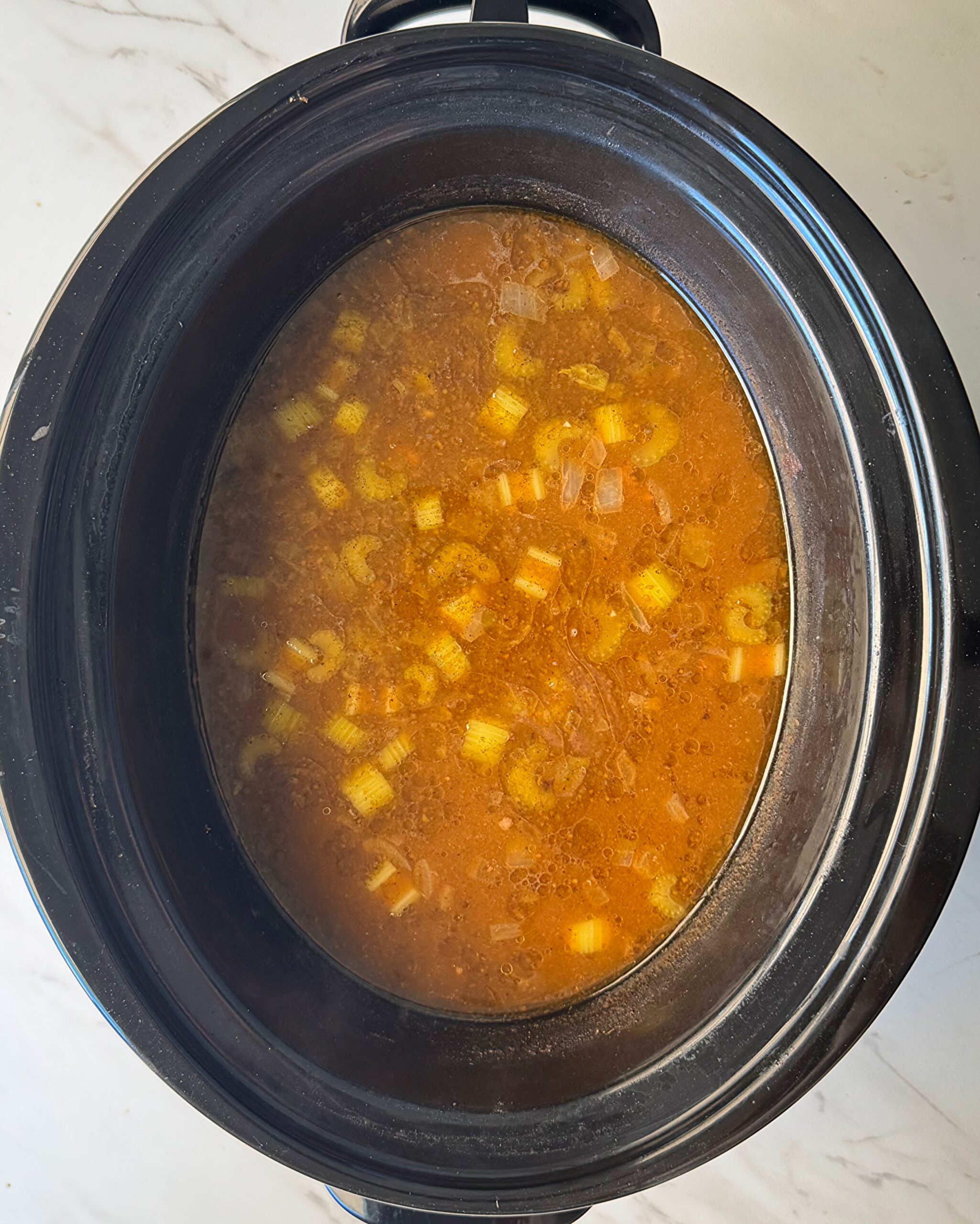 overhead shot of uncooked Beef Pumpkin Orzo Soup in a black slow cooker