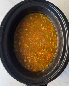 overhead shot of cooked Beef Pumpkin Orzo Soup in a black slow cooker