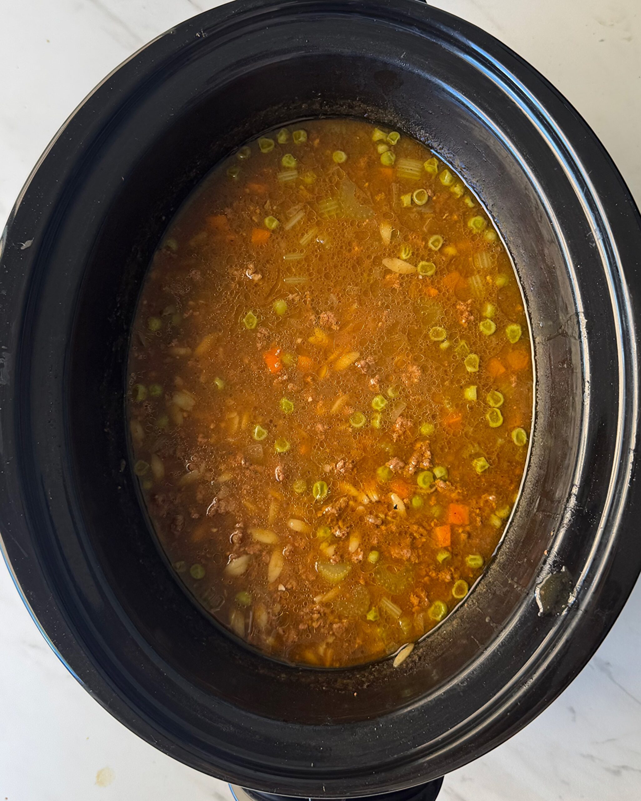 overhead shot of cooked Beef Pumpkin Orzo Soup in a black slow cooker