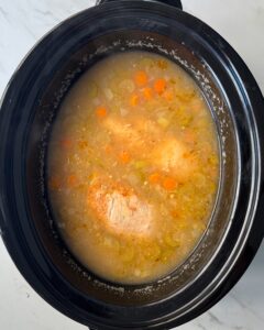 overhead shot of cooked Chicken and Rice Soup in a black slow cooker with chicken not shredded yet