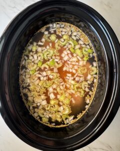 overhead shot of uncooked Chicken and Rice Soup in a black slow cooker with chicken not shredded yet