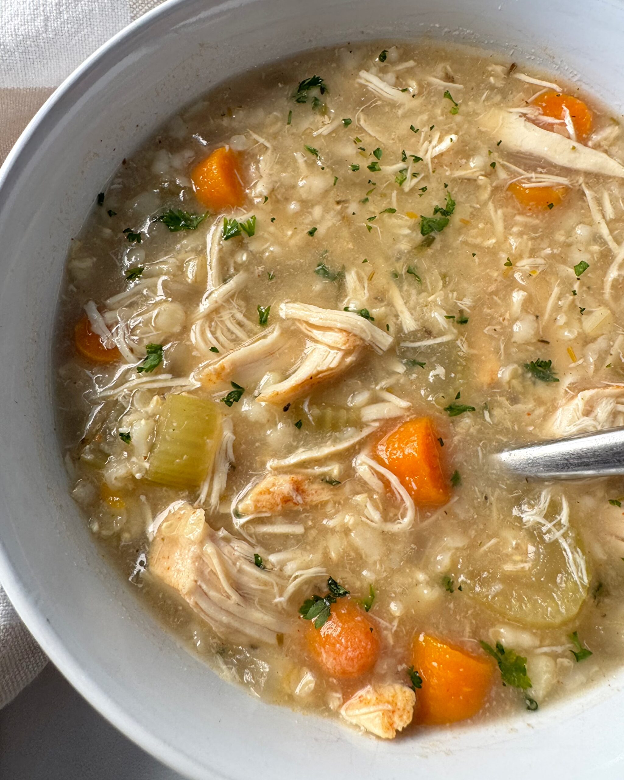 overhead shot of cooked Chicken and Rice Soup in a whit bowl with a silver spoon