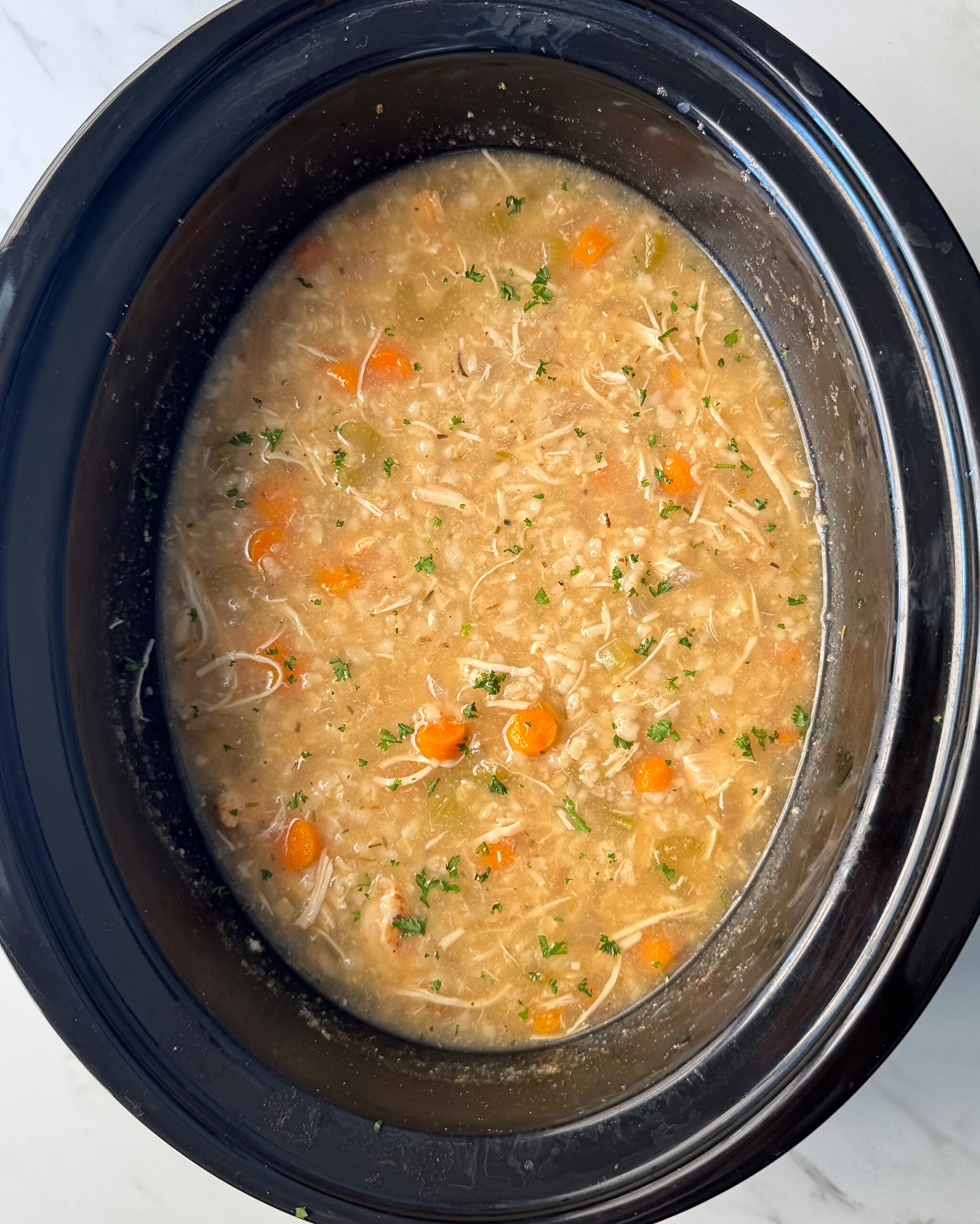 overhead shot of cooked Chicken and Rice Soup in a black slow cooker.