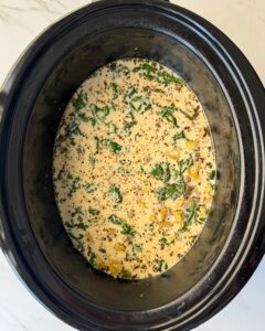 overhead shot of cooked creamy Ground Beef Pasta in a black slow cooker with the pasta and cream added