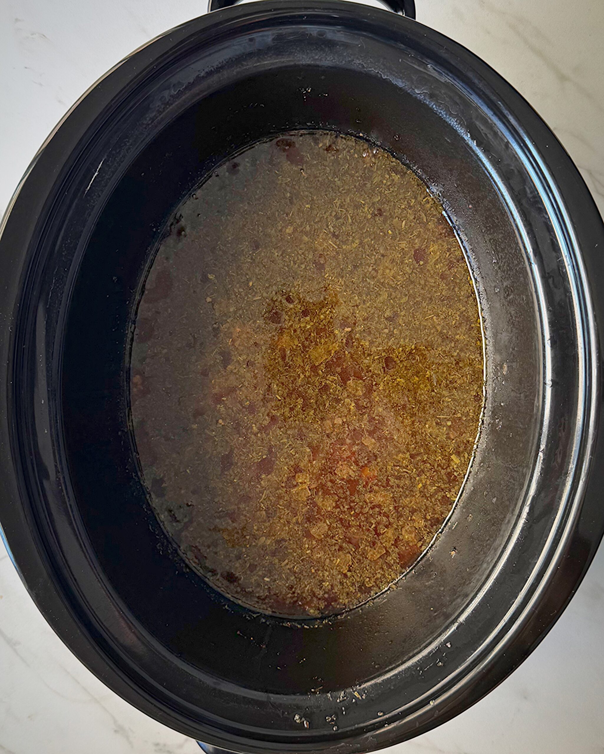 overhead shot of cooked creamy Ground Beef Pasta in a black slow cooker without the pasta and cream added