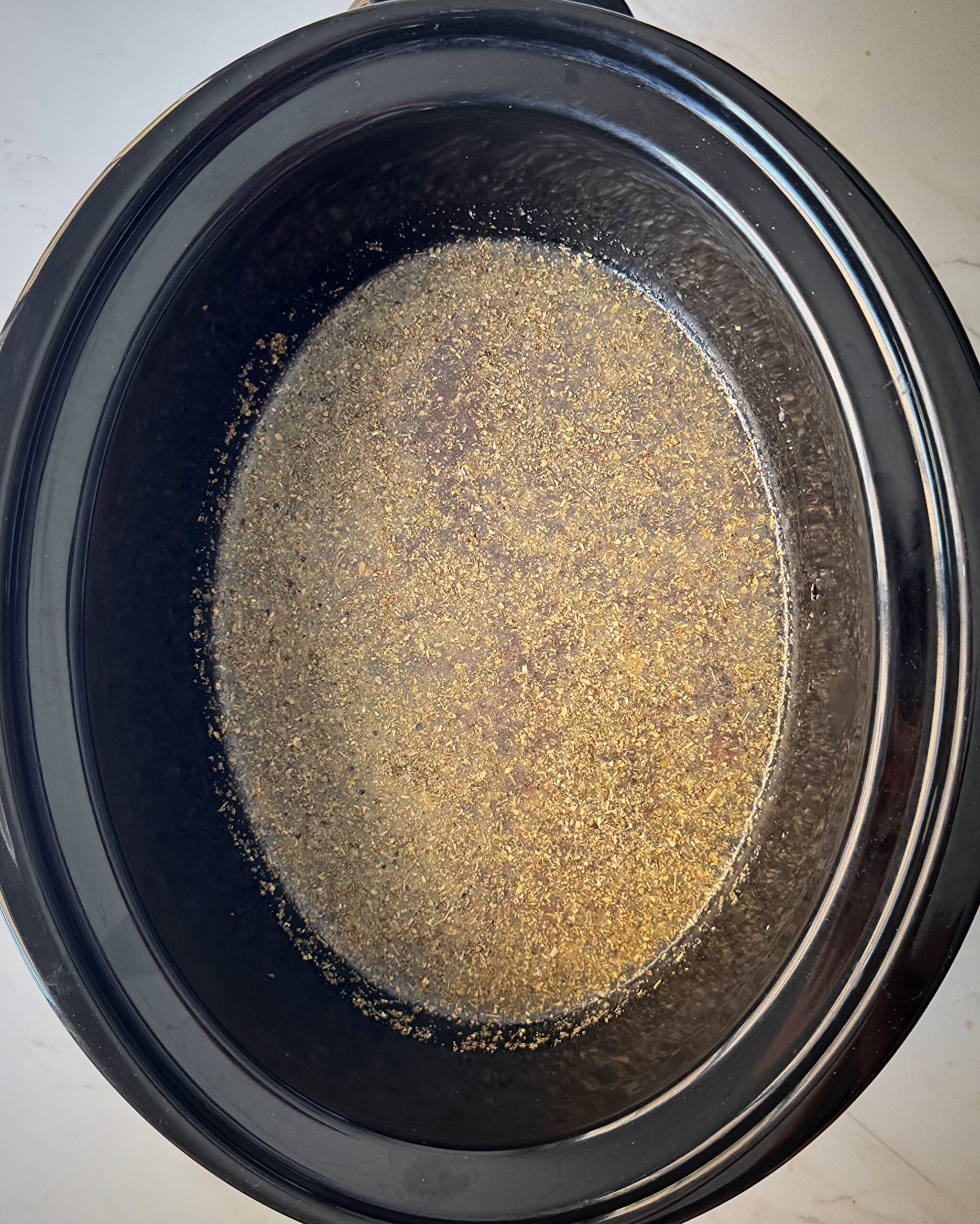 overhead shot of uncooked creamy Ground Beef Pasta in a black slow cooker without the pasta and cream added