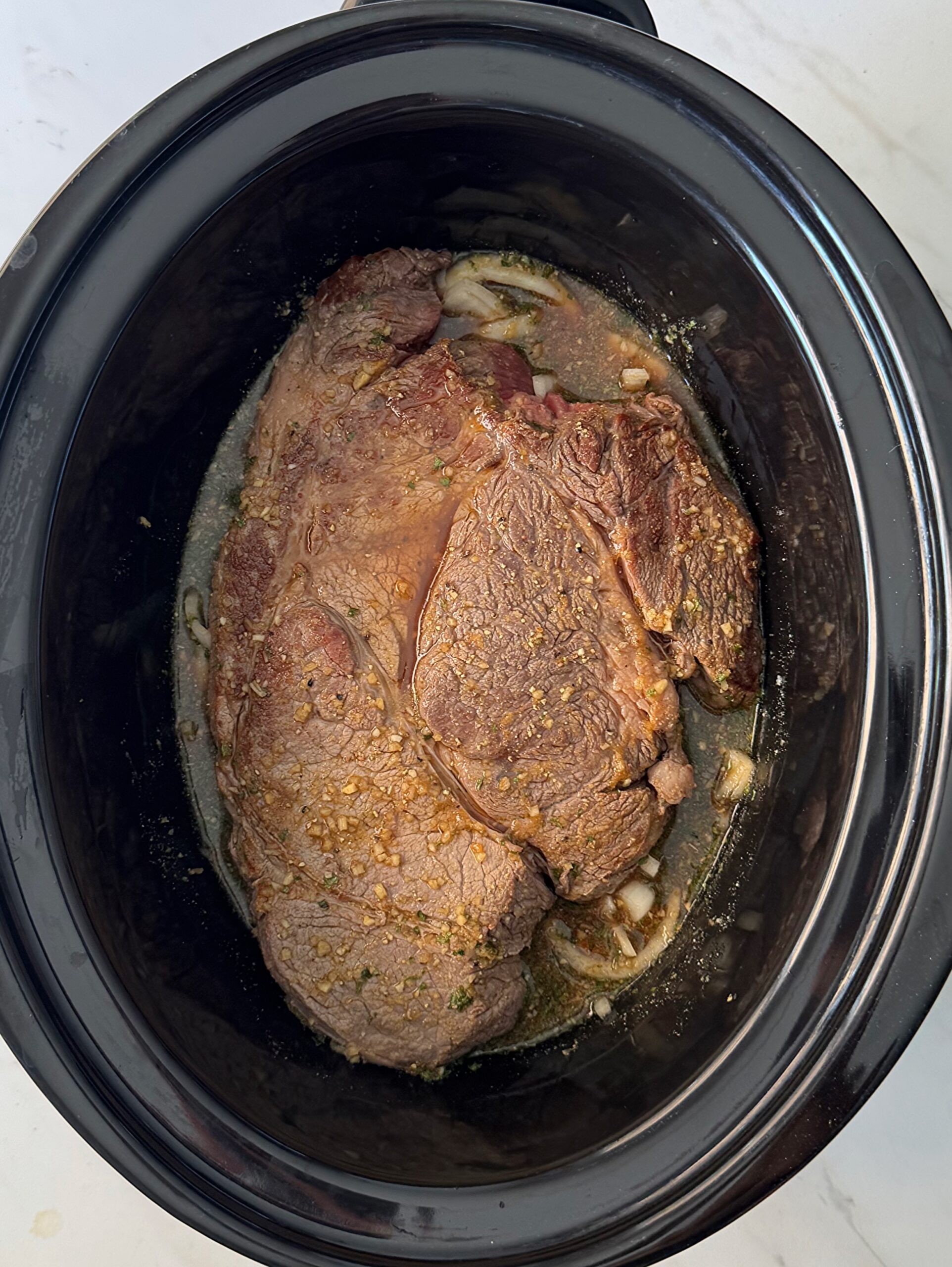 overhead shot of uncooked French onion Pot Roast in a black slow cooker