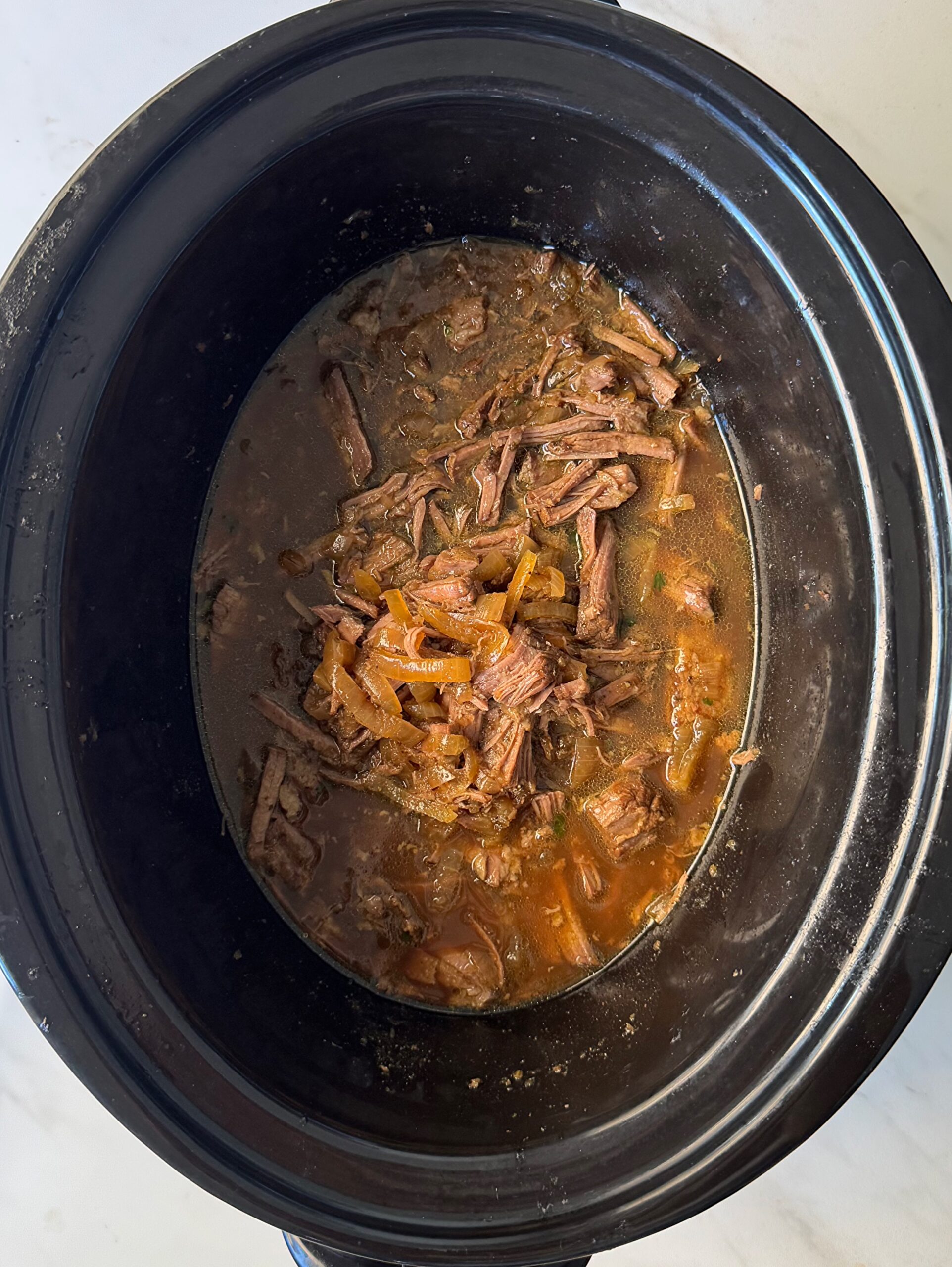 overhead shot of cooked, shredded French onion Pot Roast in a black slow cooker