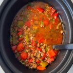 overhead shot of cooked Stuffed Pepper Soup in a black slow cooker with a black spoon in it