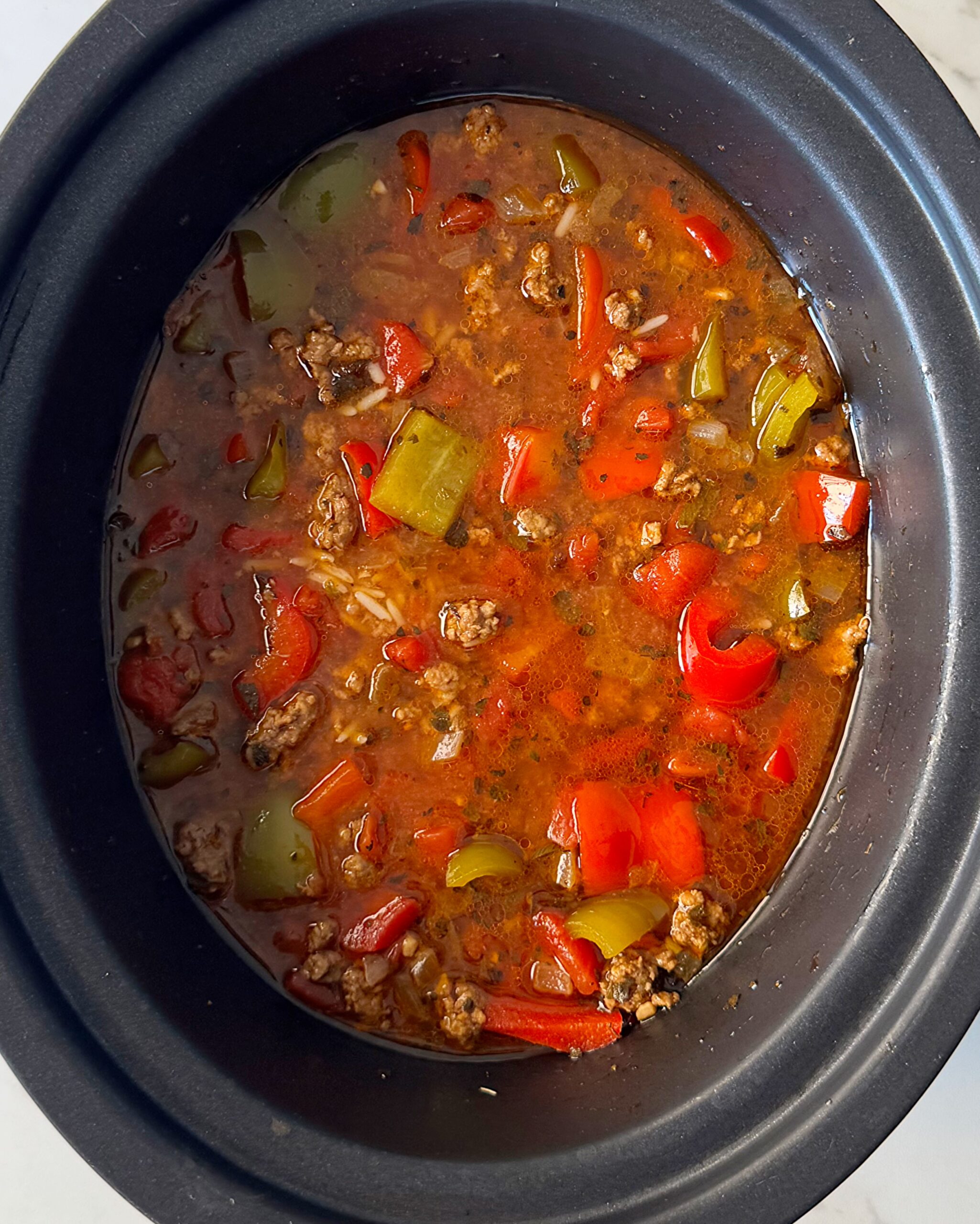 overhead shot of cooked Stuffed Pepper Soup with rice added in a black slow cooker
