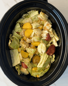 overhead shot of uncooked cabbage, sausage, and potatoes in a black slow cooker