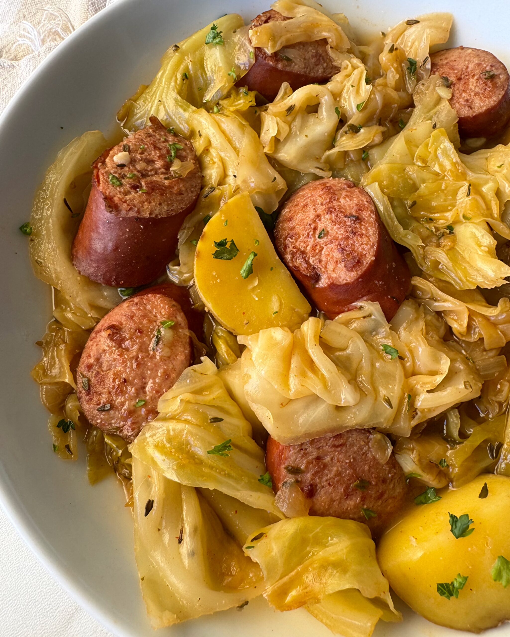 overhead shot of cooked cabbage sausage potatoes in a white bowl