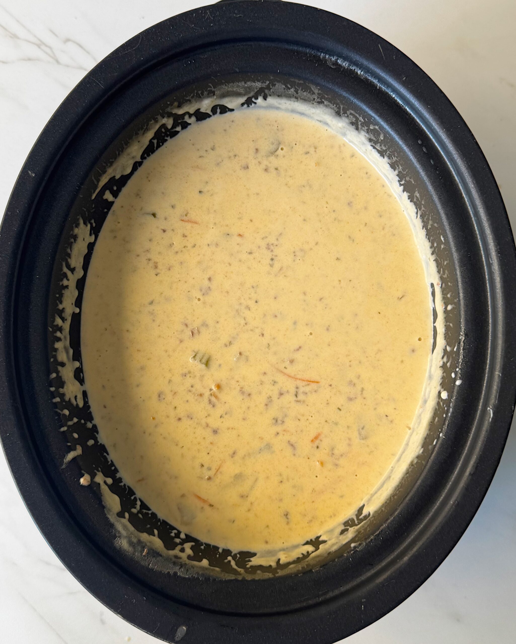 overhead shot of cooked cheeseburger soup in a black slow cooker with the cheese and cream added