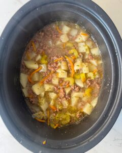 overhead shot of cooked cheeseburger soup in a black slow cooker without the cheese and cream added