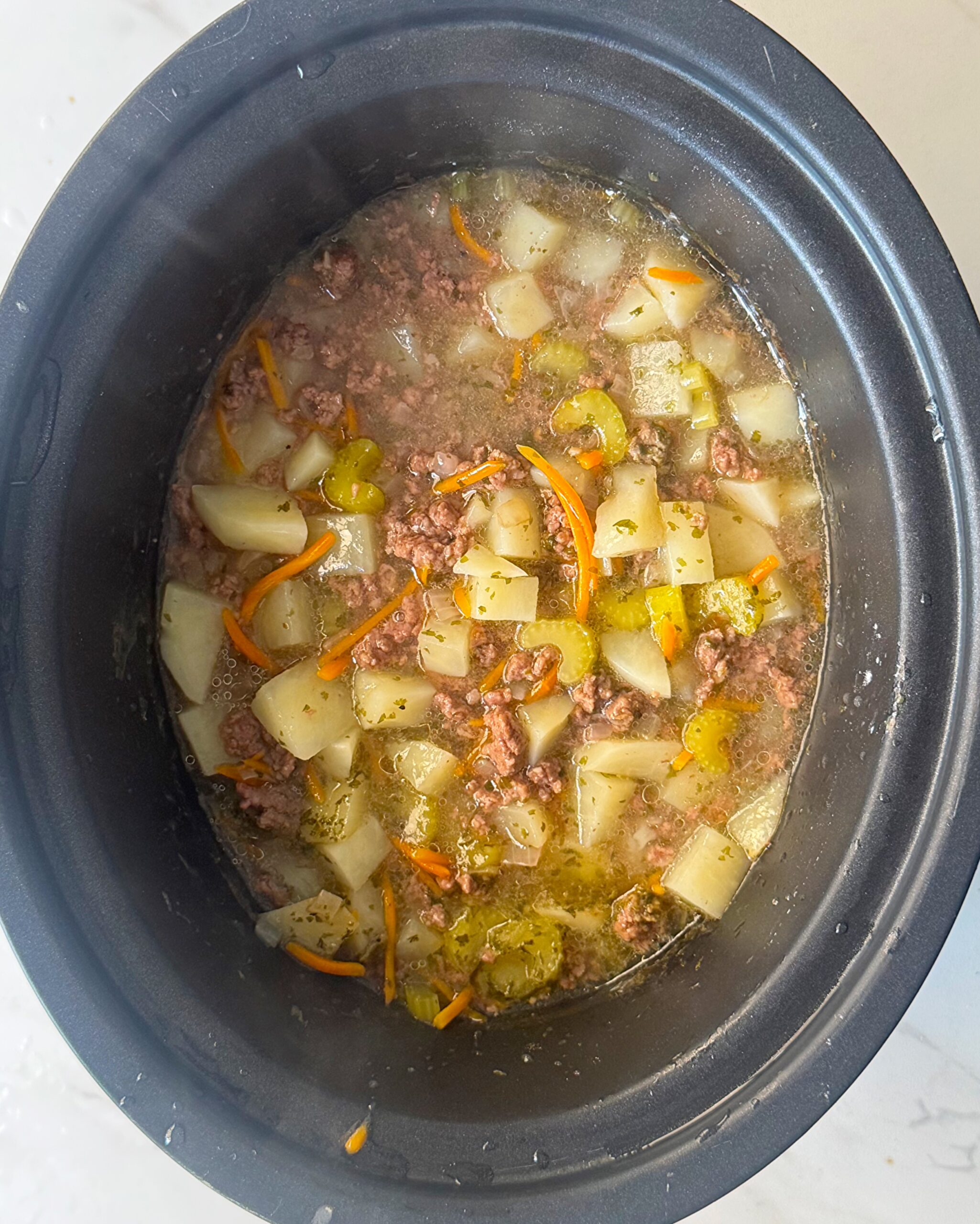 overhead shot of cooked cheeseburger soup in a black slow cooker without the cheese and cream added