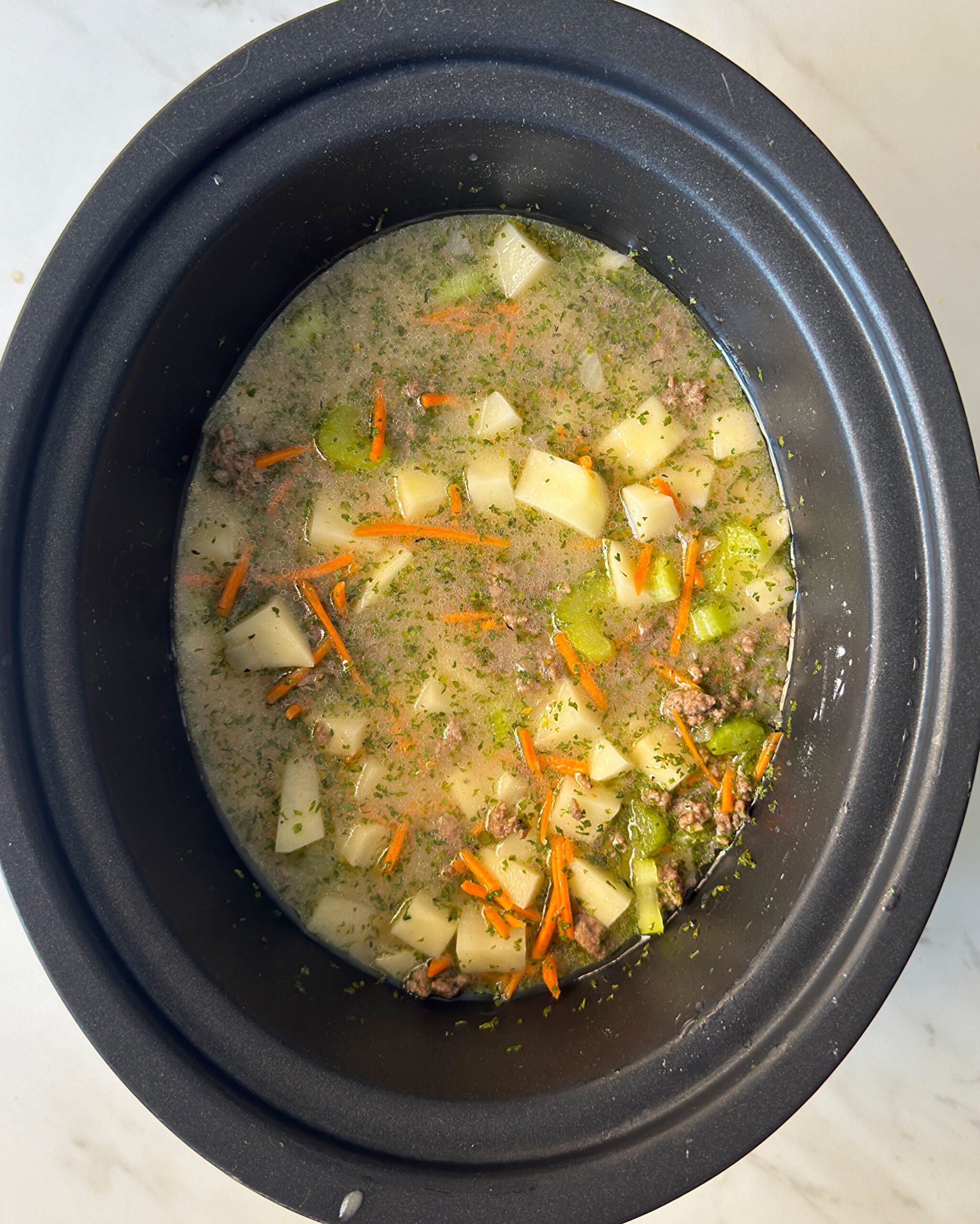 overhead shot of uncooked cheeseburger soup in a black slow cooker without the cheese and cream added