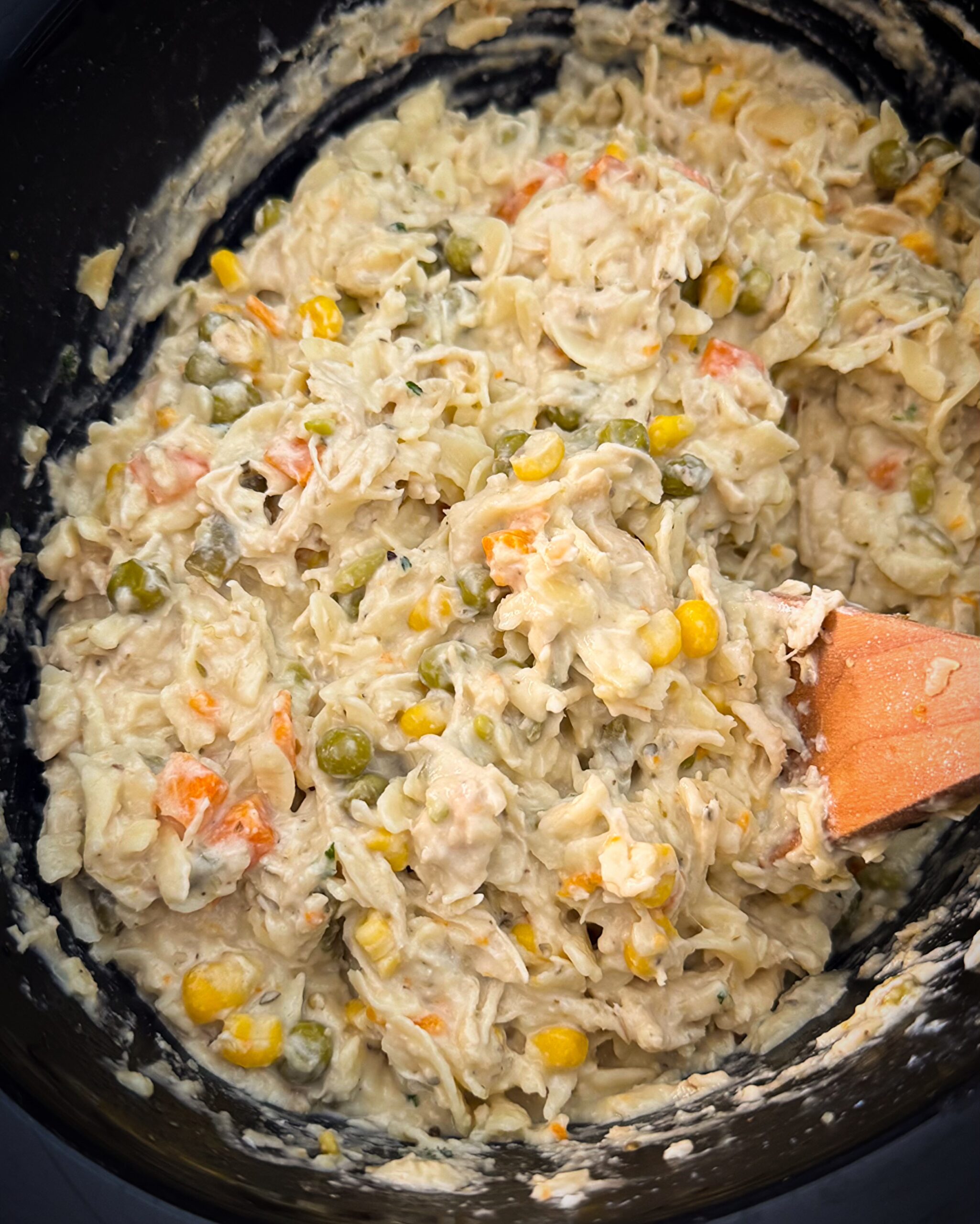 overhead shot of cooked chicken and noodles in a black slow cooker 