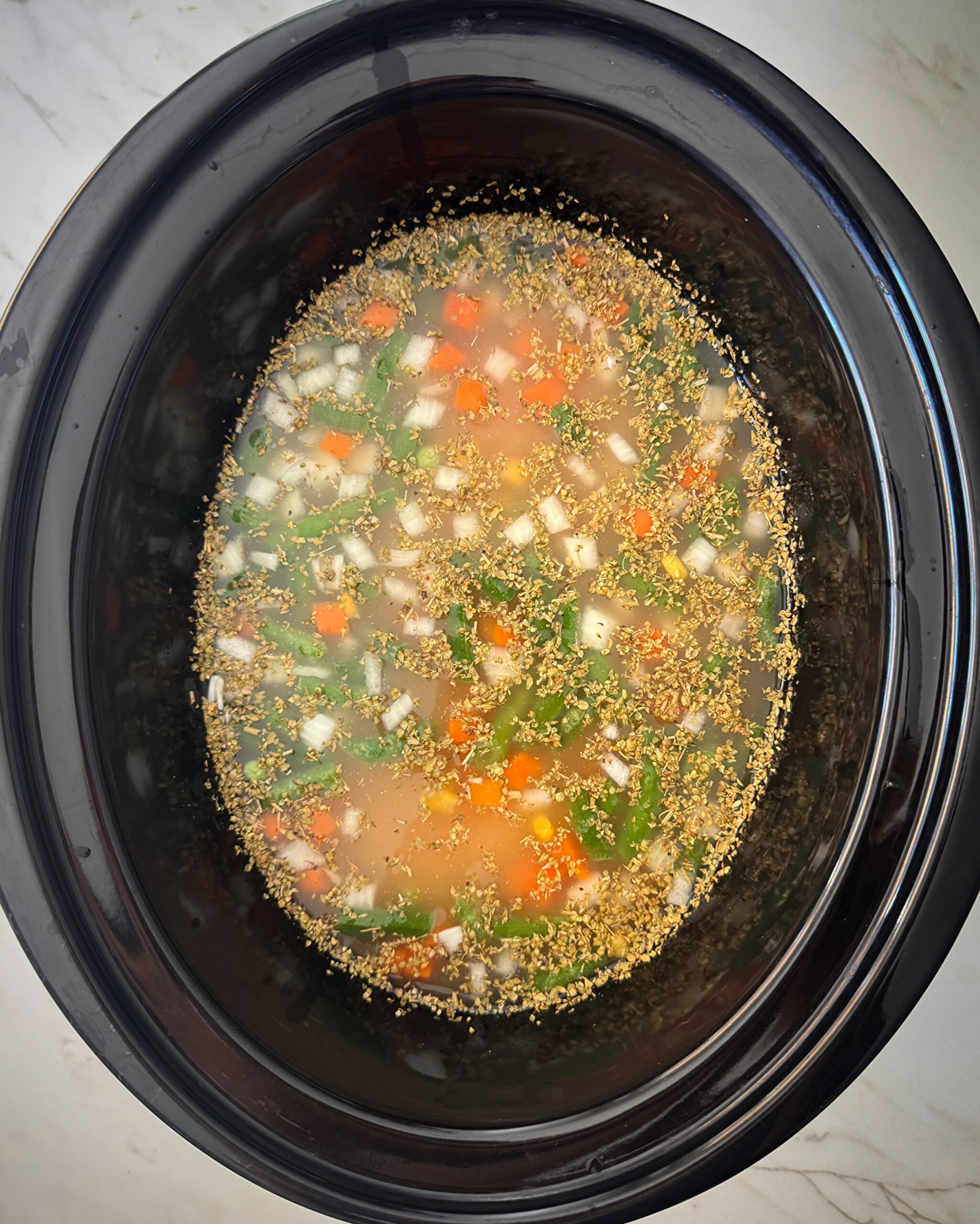 overhead shot of uncooked chicken and noodles in a black slow cooker