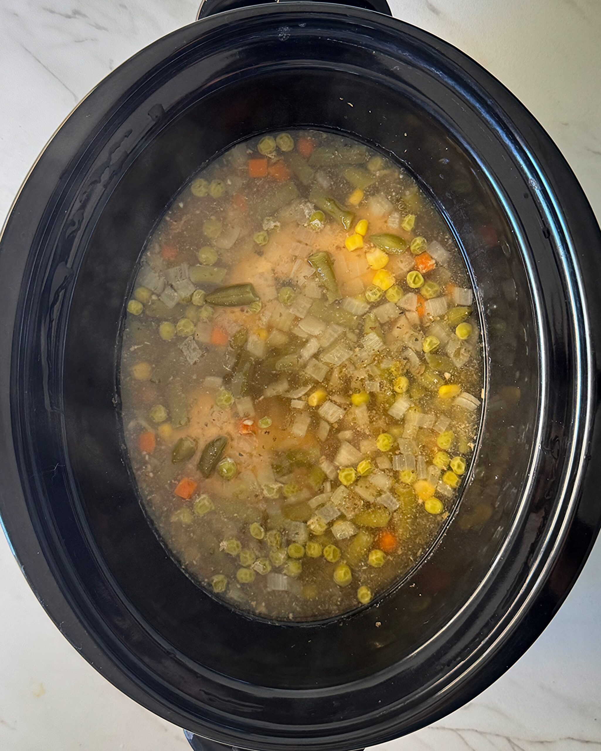 overhead shot of cooked chicken and noodles in a black slow cooker