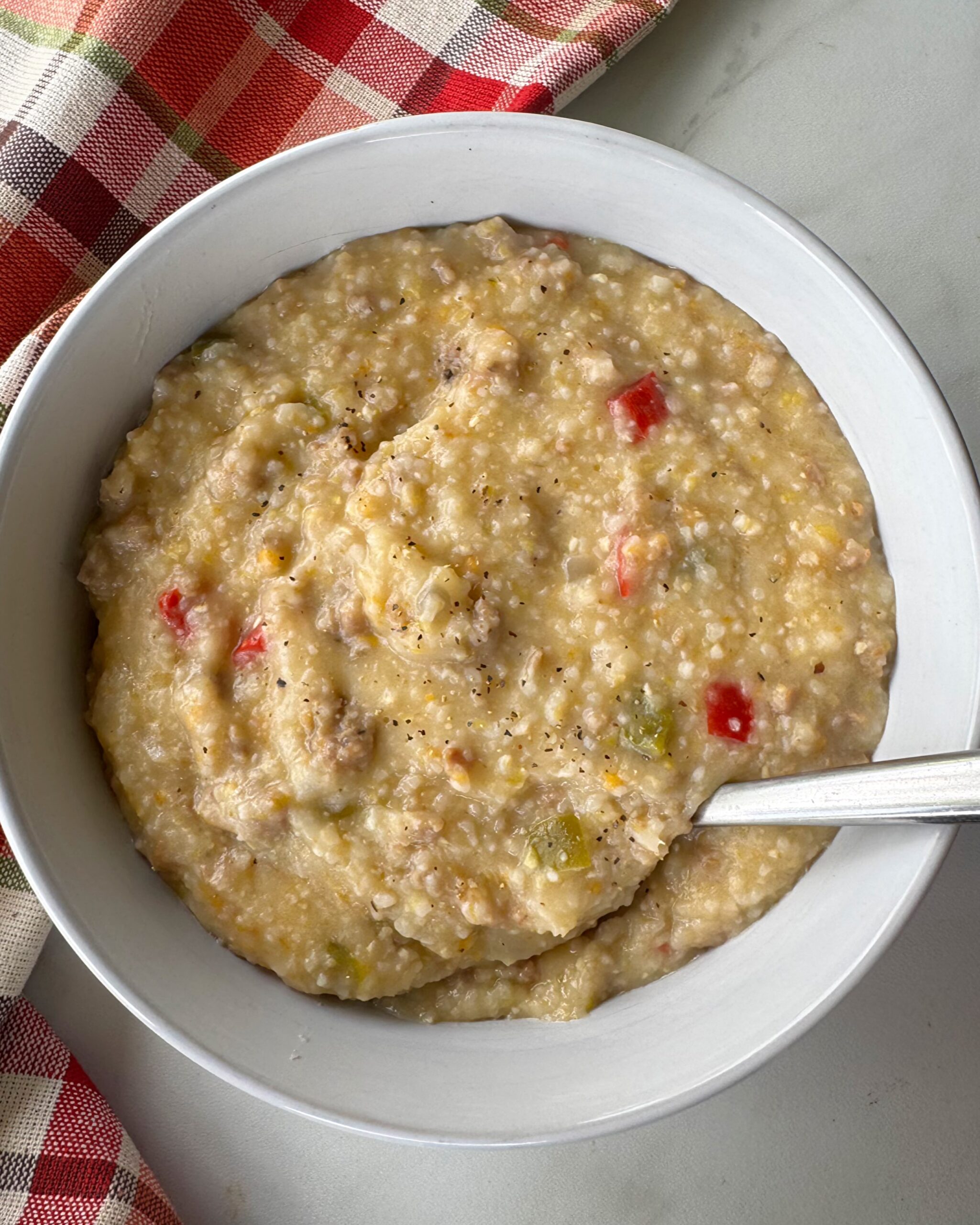 overhead shot of Crockpot Sausage Cheese Grits in a white bowl with a silver spoon