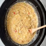 overhead shot of cooked sausage cheese grits in a black slow cooker with a wooden spoon